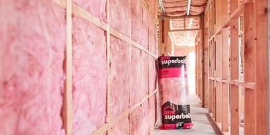 Pink fiberglass insulation installed between wooden studs in a building under construction.