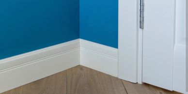 Clean corner of a room with blue walls, white trim, and wooden floor.