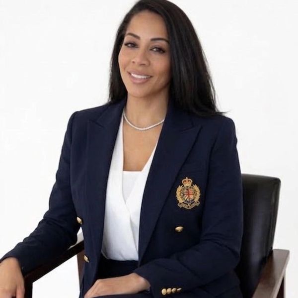 Confident woman in a navy blazer with a crest emblem, seated and smiling.