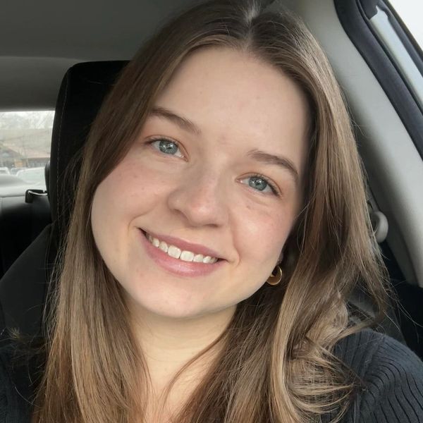 Smiling young woman with long brown hair inside a car.
