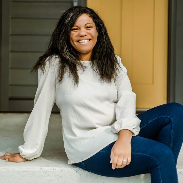 Smiling woman sitting on steps, wearing white blouse and blue jeans.