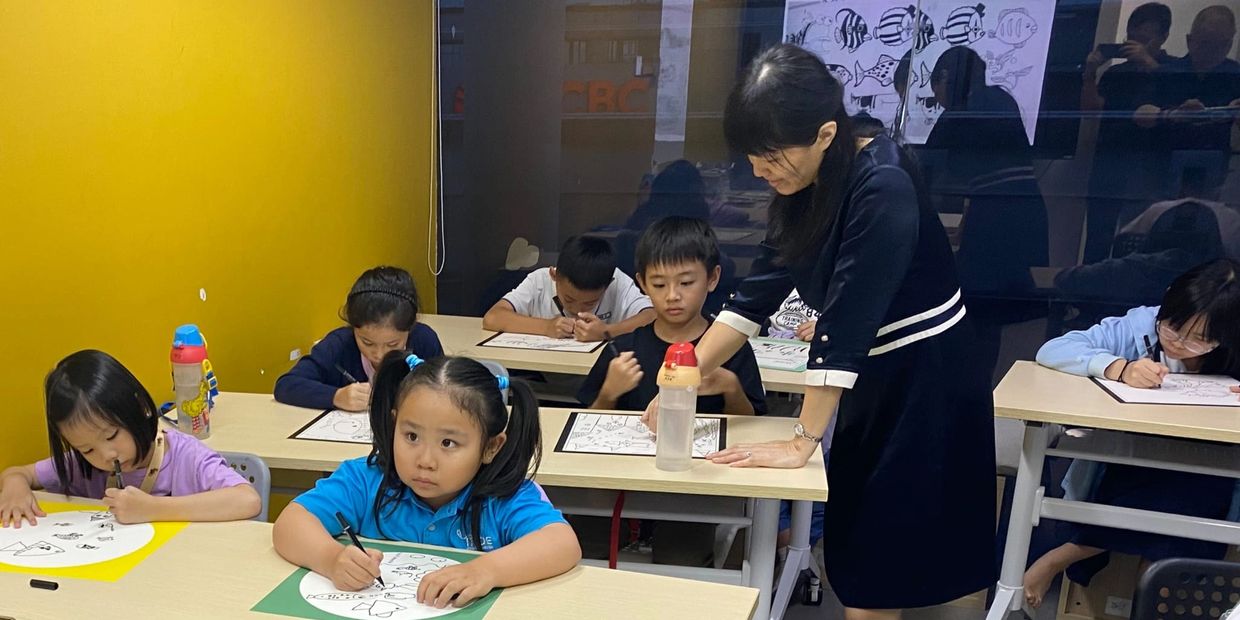Children attentively drawing in a classroom with a teacher assisting one student.