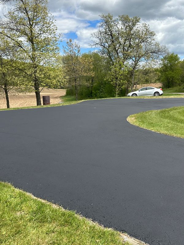 Freshly paved driveway in a green suburban area under a cloudy sky.