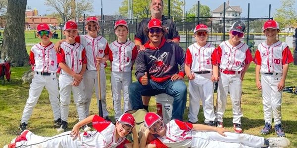 Youth baseball team posing with coaches outdoors on a sunny day.