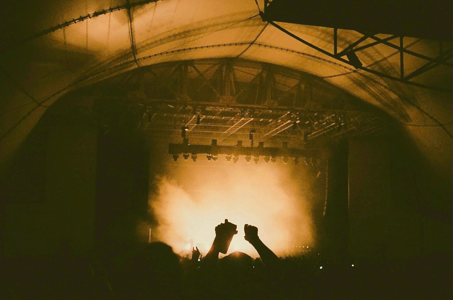 Crowd at a concert with raised hands against bright stage lights.