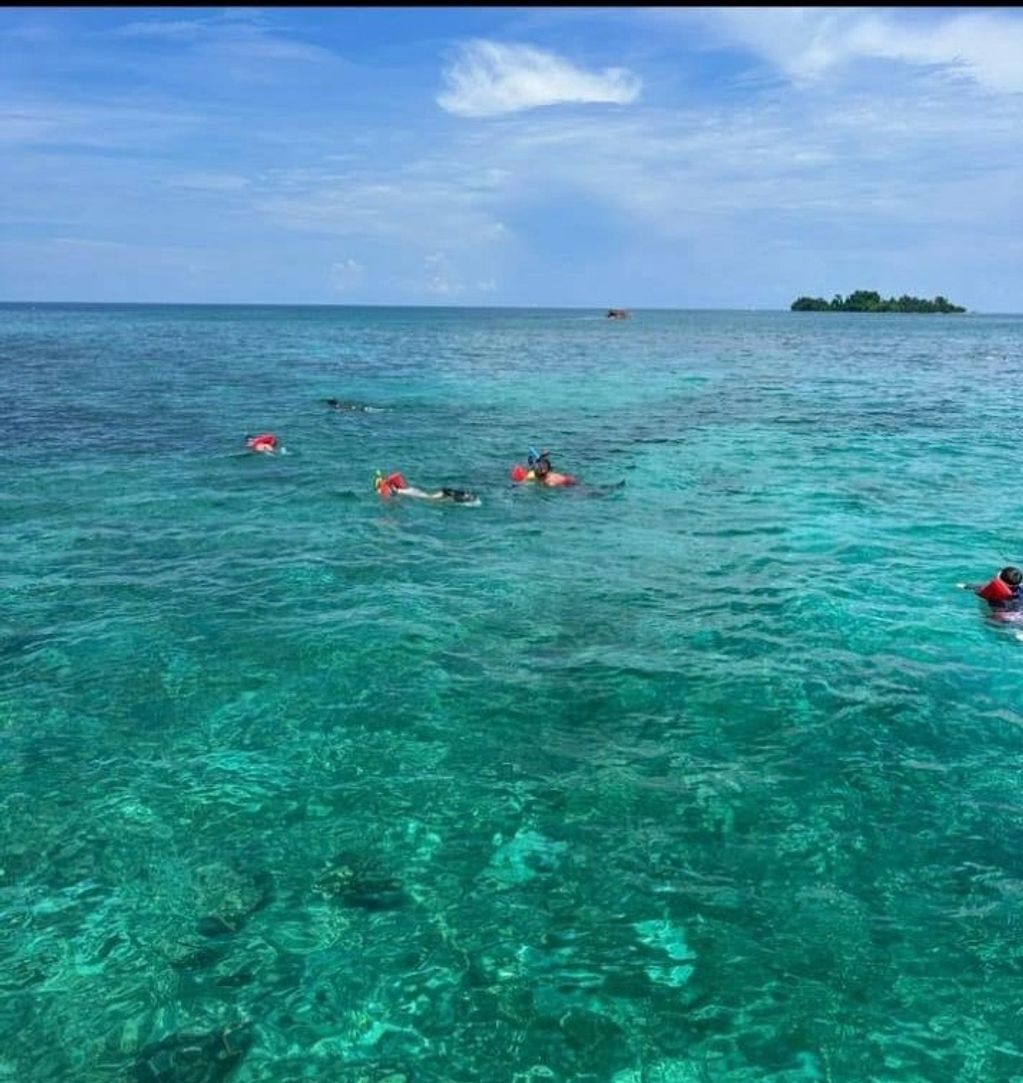 People snorkeling in clear turquoise ocean water near a small island.