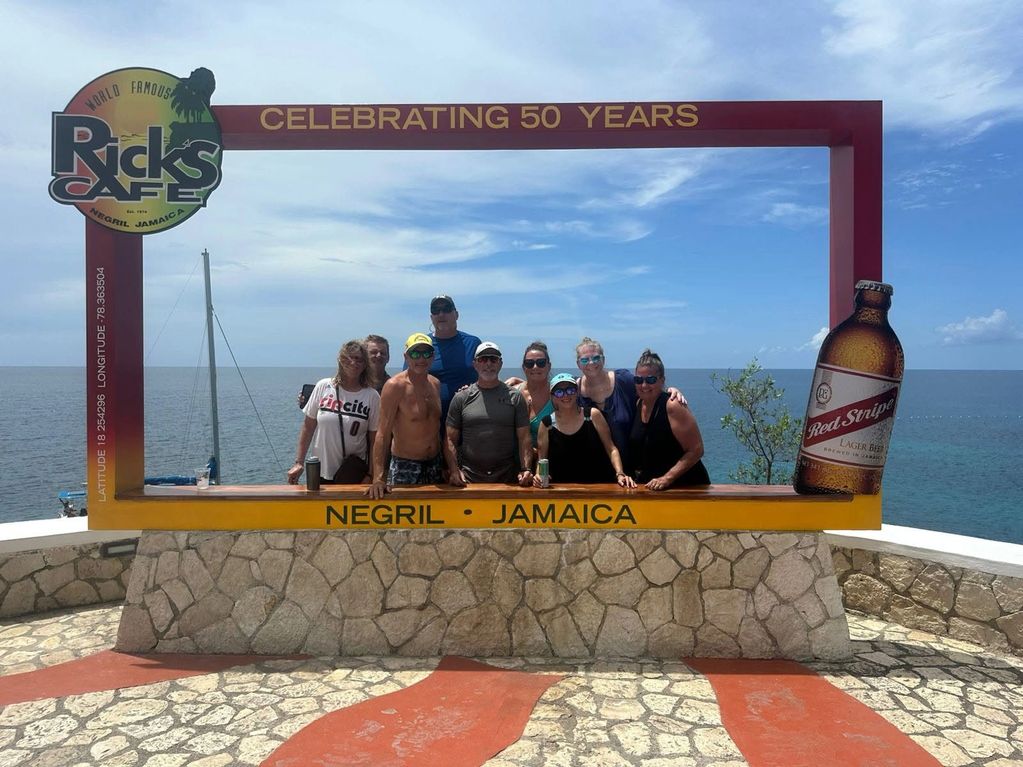 Group of people posing at Rick's Cafe frame with ocean backdrop in Negril, Jamaica.