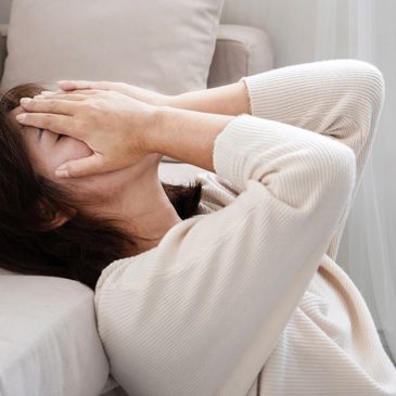 Woman lying down with hands covering her face, showing distress.