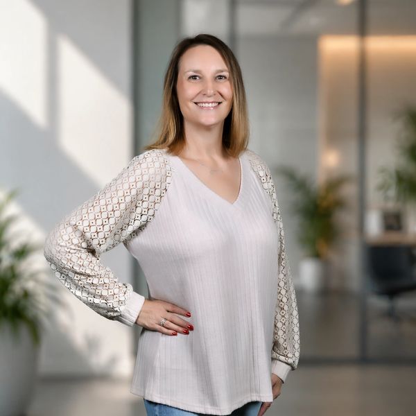 Smiling woman in a white blouse with patterned sleeves stands confidently indoors.