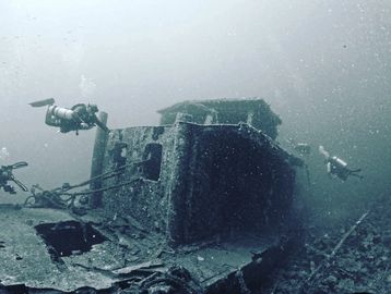 Scuba divers exploring a sunken shipwreck underwater.
