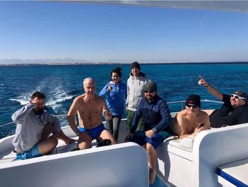 Seven friends enjoying a sunny boat ride on clear blue waters.