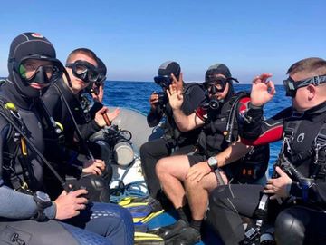 A group of scuba divers on a boat ready for a dive in clear blue waters.