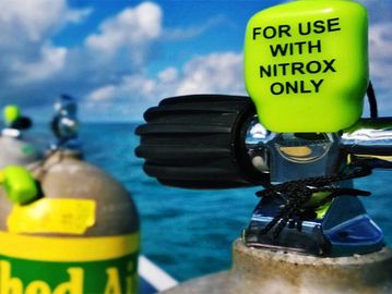 Scuba diving tanks labeled for Nitrox use on a boat with ocean background.