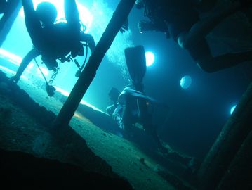 Scuba divers exploring an underwater shipwreck illuminated by natural light.