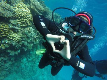Scuba diver underwater making a heart shape with hands near coral reef.