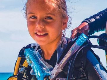 Young girl in scuba diving gear smiling by the ocean.