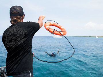 A person throws a lifebuoy to a swimmer in the sea.
