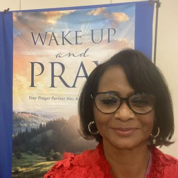 Woman smiling in front of a 'Wake Up and Pray' poster.