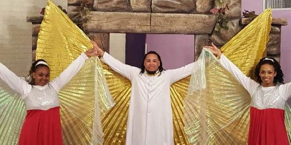 Three people in white and red attire with golden wings on stage.