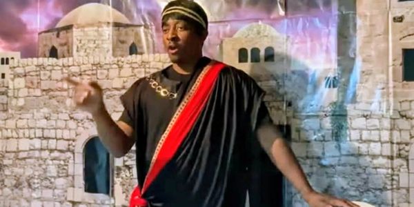 Man dressed in historical costume with a stone wall backdrop.