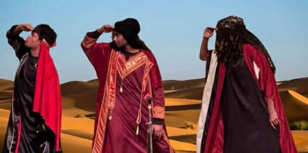 Three men in traditional robes looking into the distance in a desert.