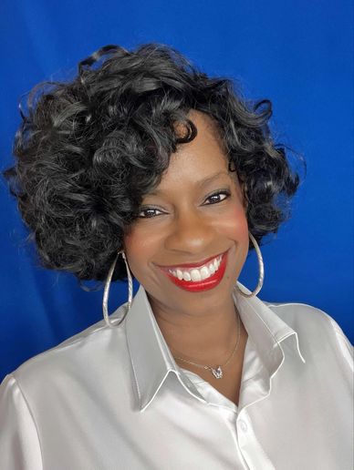 Woman with curly hair smiles brightly against a blue backdrop.