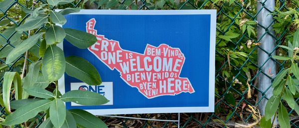 Sign posted against a chain link fence, with a map of Somerville enclosing the words "Everyone is We