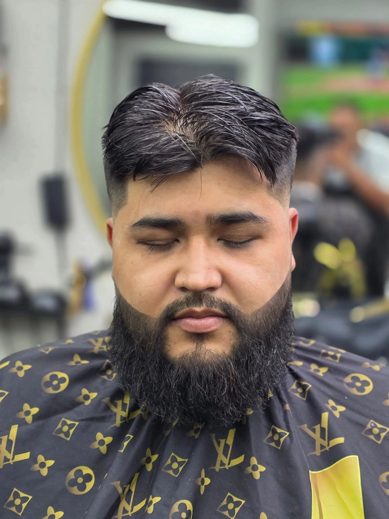 Man with a fresh haircut and neatly trimmed beard sitting in a barbershop.
