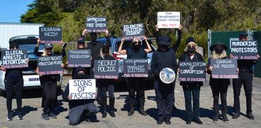 Protesters hold signs against fascism and injustice outdoors.