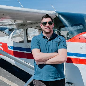 Man in sunglasses standing confidently in front of a small airplane on a sunny day.