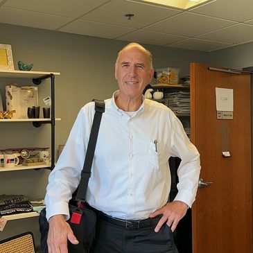 Smiling man in white shirt with black bag in an office setting.