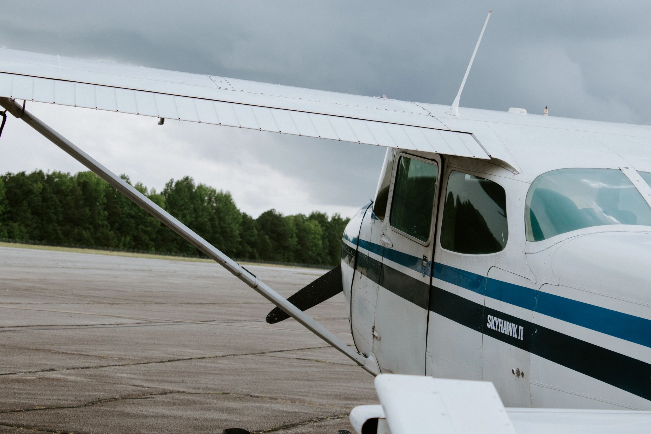 Close-up of a Cessna Skyhawk II airplane wing and cockpit on a cloudy day.