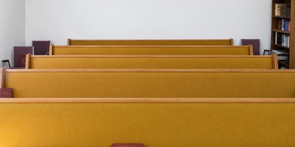Empty wooden pews with mustard-yellow cushions in a chapel.