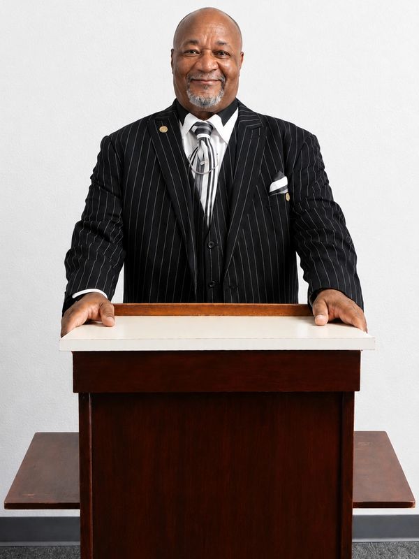Well-dressed man standing at a podium, smiling.