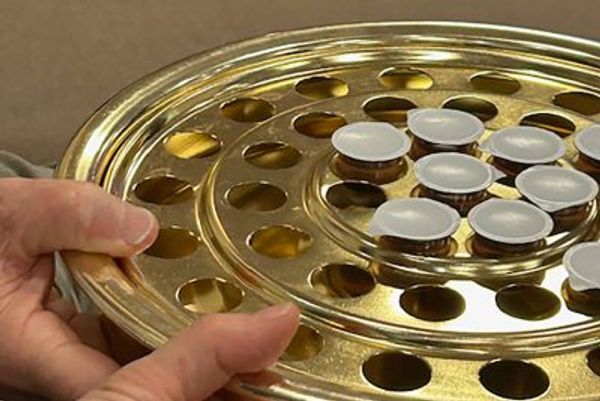 Person holding a gold communion tray with cups.