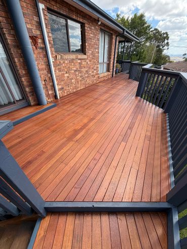 Newly polished wooden deck attached to a brick house with black railing.