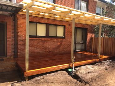 New wooden deck with pergola attached to a brick house.