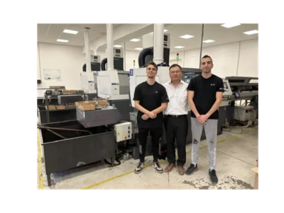 Three men standing in a factory next to machinery.