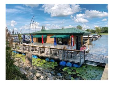 A lakeside building with colorful umbrellas on its deck under a partly cloudy sky.