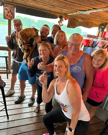 Group of friends smiling and holding small shot glasses in a rustic setting.
