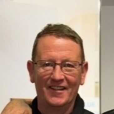 Smiling man with glasses and short hair indoors.