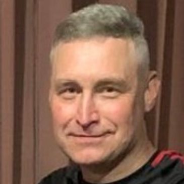 Smiling man with short gray hair wearing a black and red shirt.