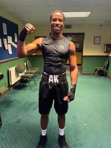 A muscular man in boxing attire flexes his arm in a gym room.