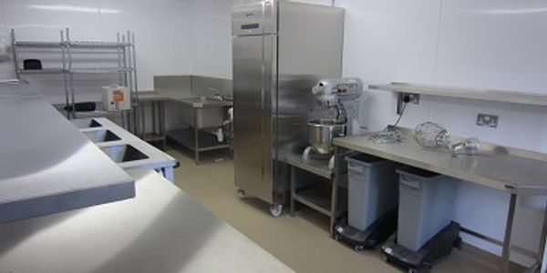 Part view of a commercial kitchen with stainless steel fabricated tables and upright refrigerator