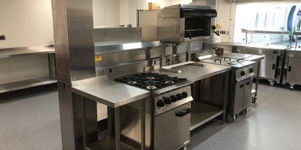 A centre island of stainless steel cooking equipment with other appliances around the outer walls
