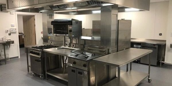 Centre island of stainless steel cooking appliances in a commercial kitchen with extraction canopy