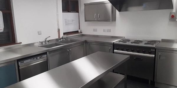 Corner view of kitchen with centre food preparation table, sink, dishwasher, cooker & storage units