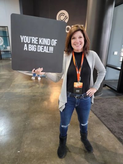 Woman holding a sign that says 'YOU'RE KIND OF A BIG DEAL!!!' indoors.