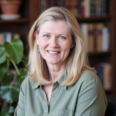 Smiling blonde woman in green shirt with bookshelf background.