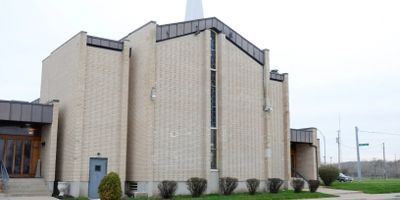 Modern beige brick church building with tall windows and greenery.